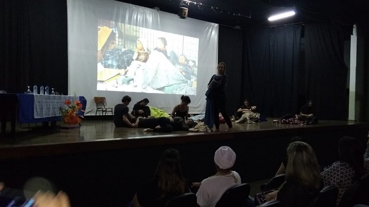 Dez atores, uma delas de pé, segurando um bebé. Os que estão sentados parecem segurar, como filhos, outros que estão deitatos